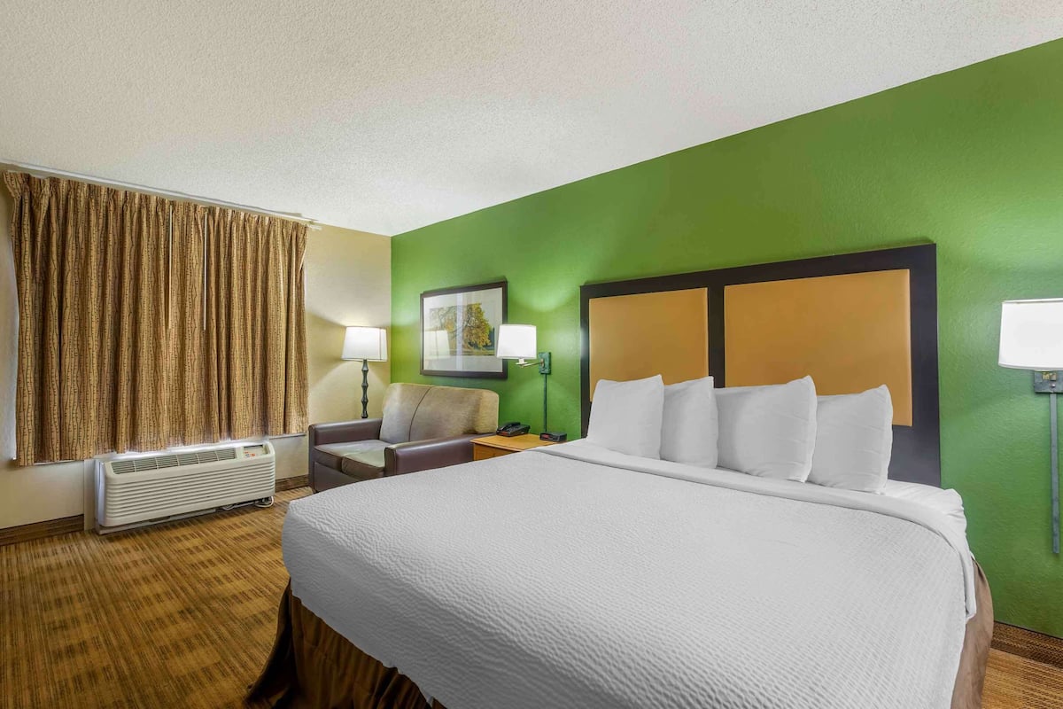 A hotel room with a large bed, a desk, a chair, a lamp, and a picture on the wall.