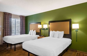 Una habitación de hotel con dos camas, un ventanal con cortinas y lámparas fijadas a la pared.