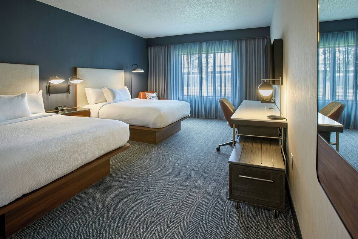 A hotel room with two beds, a desk, and a chair.