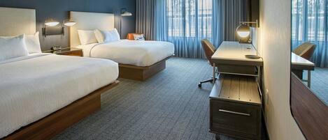 Habitación de hotel con dos camas, un escritorio y una silla.