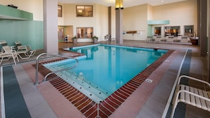 Una piscina interna con acqua cristallina, circondata da sdraio e un pavimento piastrellato.