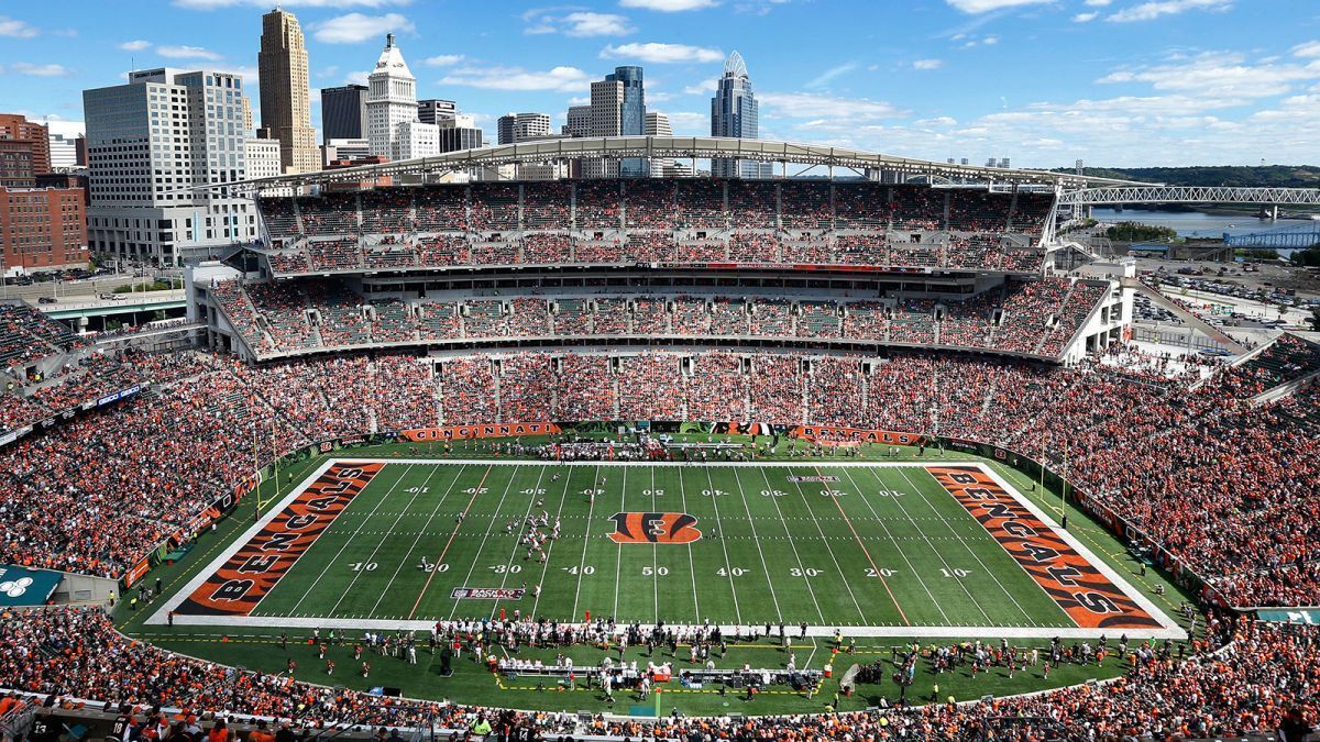 A football stadium with a large crowd, a football field, and city buildings in the background.