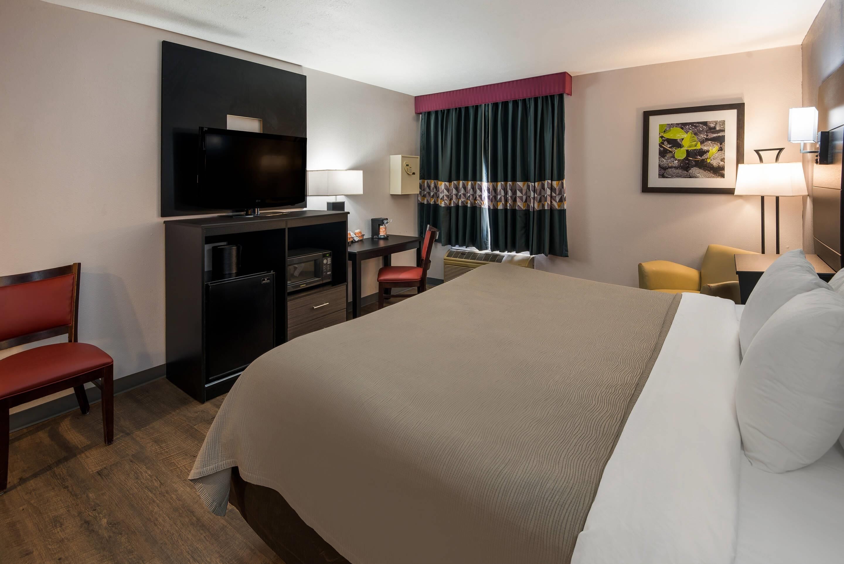 A hotel room with a large bed, a desk with a chair, a television, and a window with curtains.
