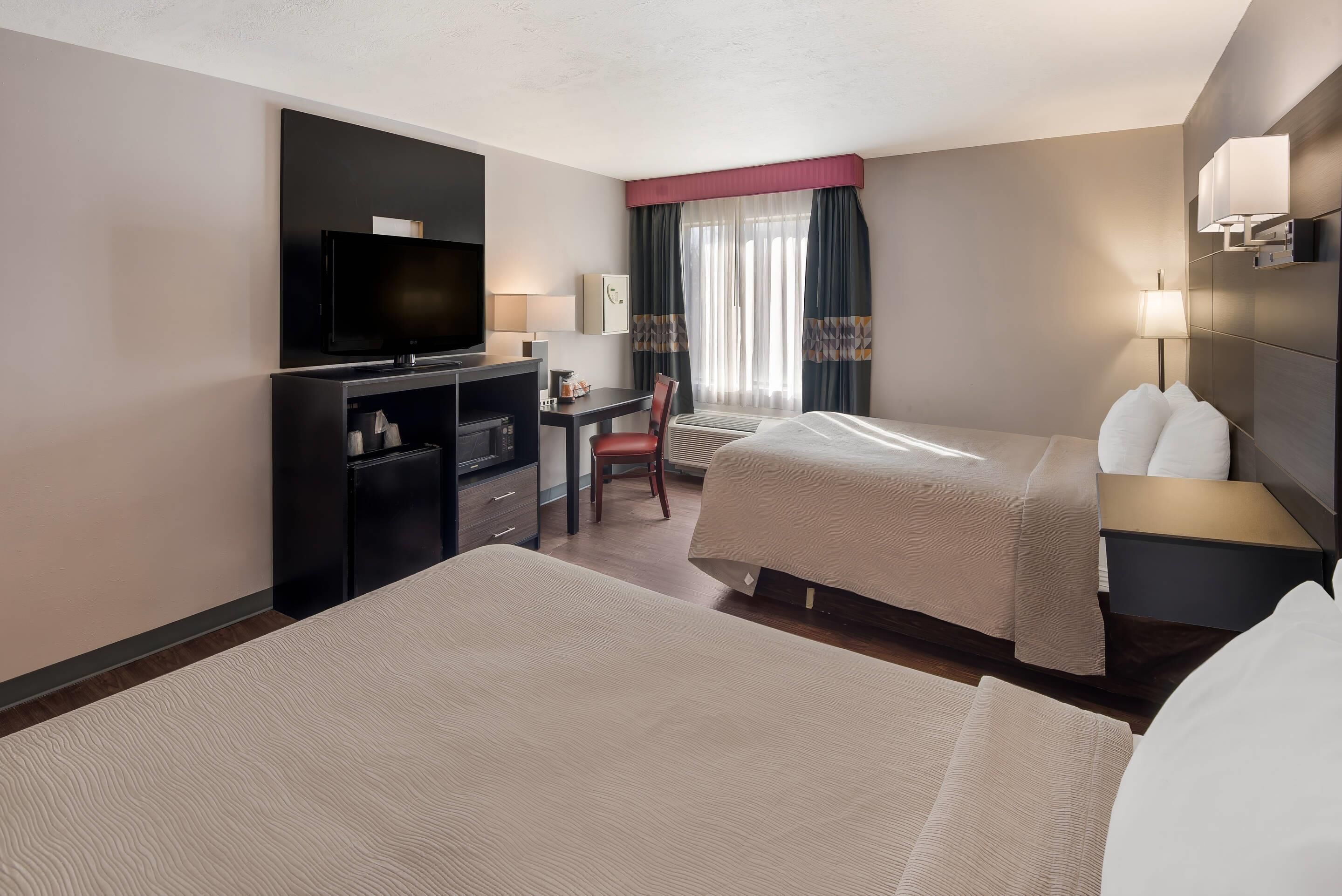 A hotel room with two beds, a desk with a television, and a chair.