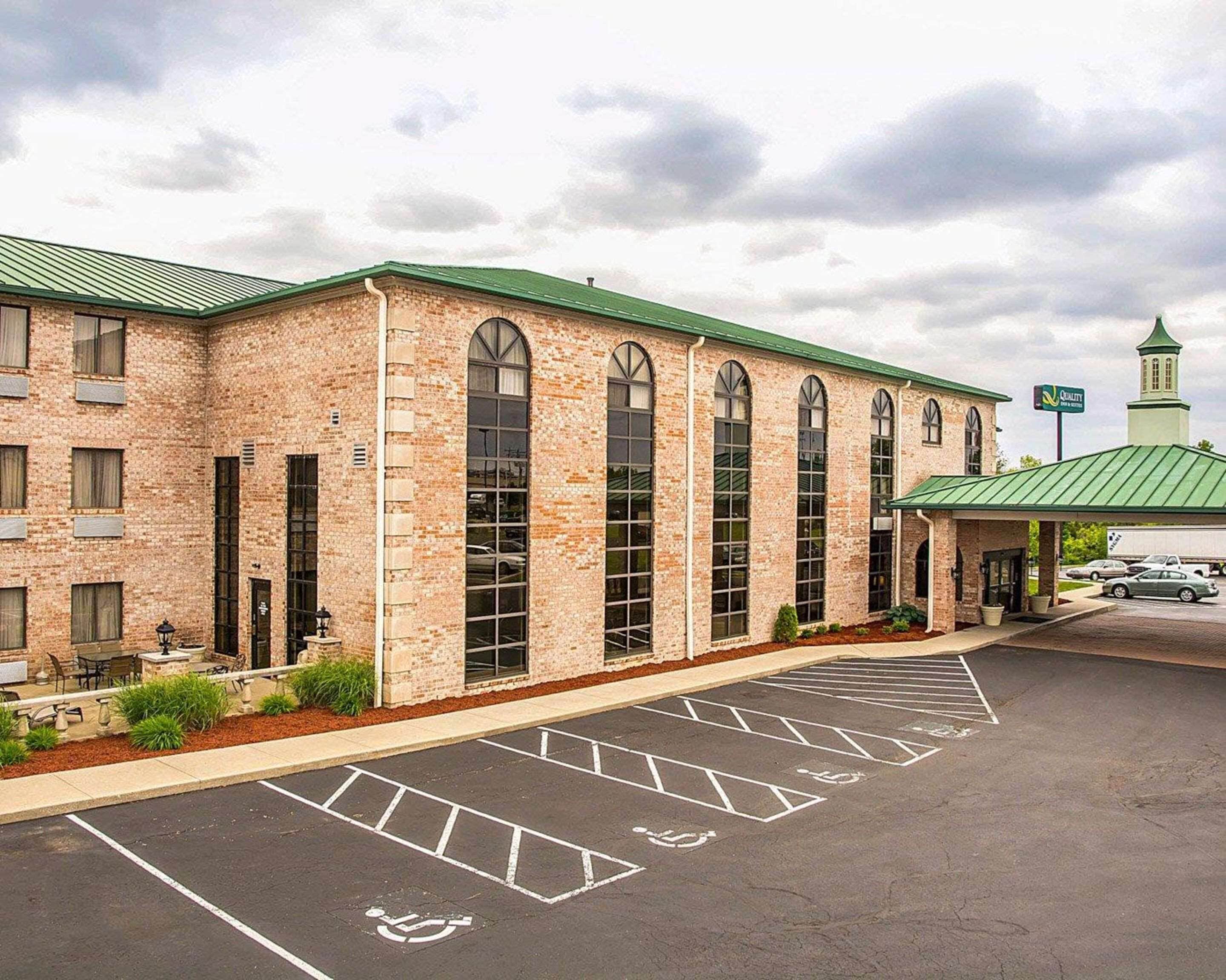 A brick building with large arched windows and a green roof. There is a parking lot with handicapped parking spaces.
