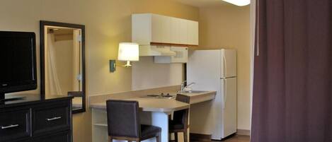 Habitación de hotel compacta con kitchenette, cama, televisión y espejo.