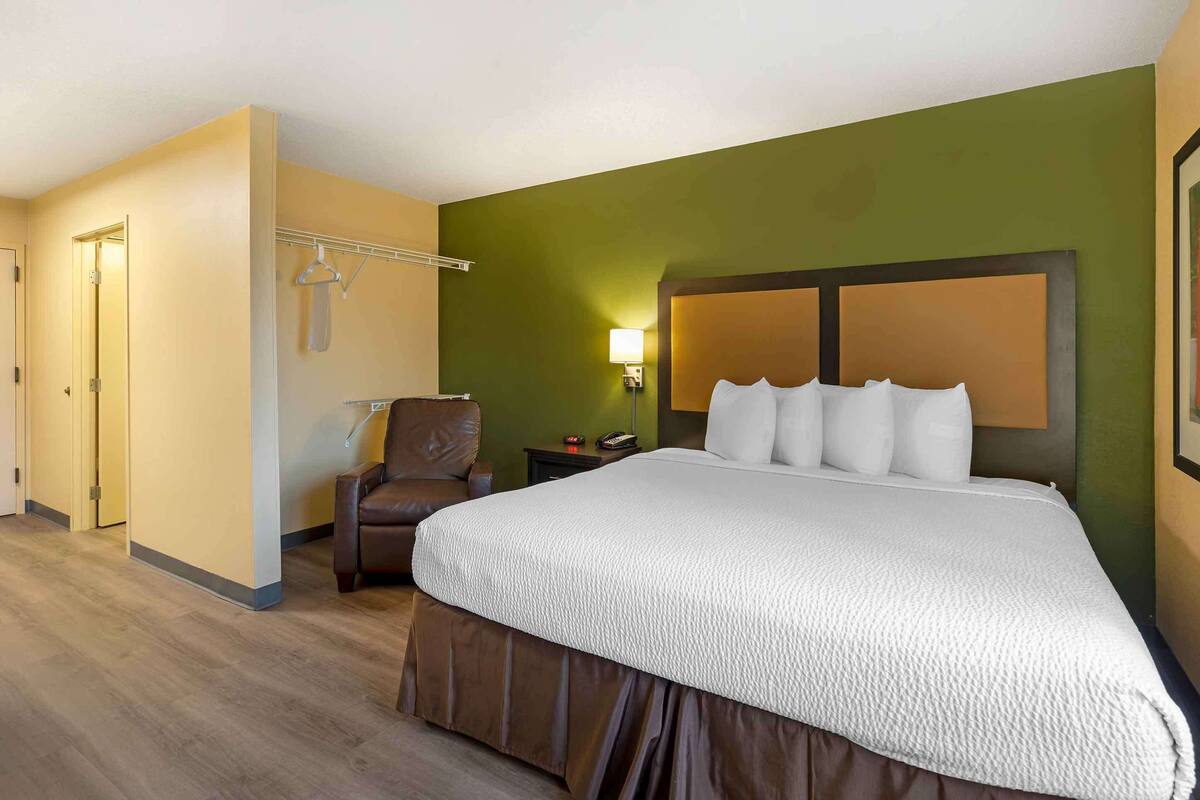 Une chambre d’hôtel avec un grand lit, une chaise, une table de chevet et une lampe fixée au mur.