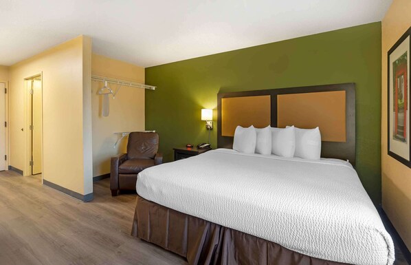 A hotel room with a large bed, a chair, a bedside table, and a wall-mounted lamp.
