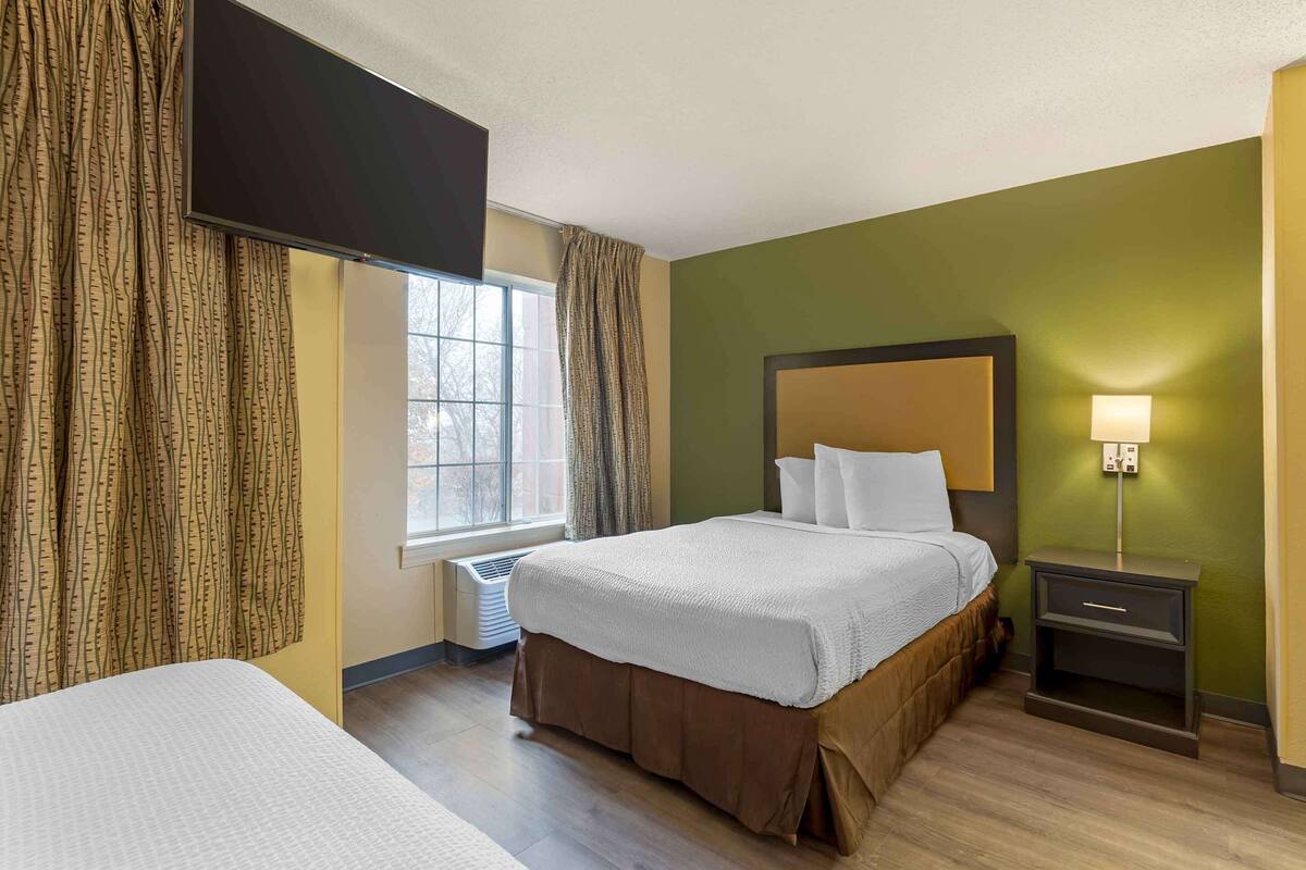 Une chambre d’hôtel avec un lit, une table de chevet, une lampe et une fenêtre avec des rideaux.