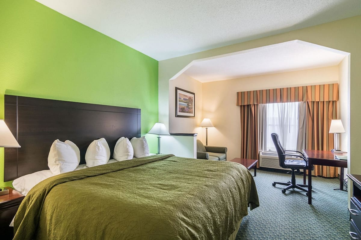 A hotel room with a bed, desk, chair, and a large window with curtains.