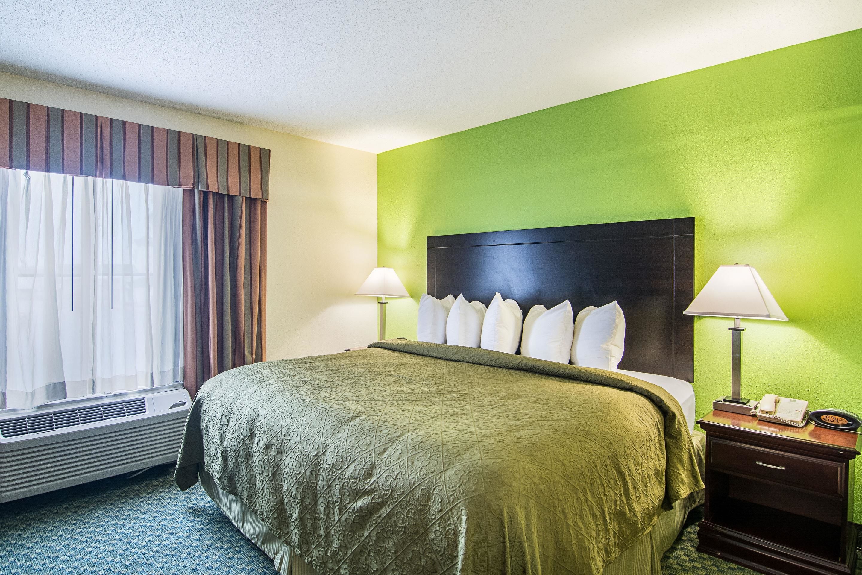 Habitación de hotel con cama, mesita de noche con lámpara, teléfono y ventana con cortinas.