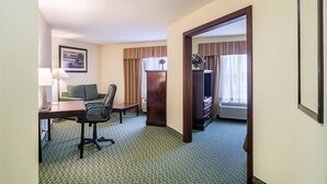 A hotel room with a desk, chair, and a bed. There is a window with curtains, a lamp, and a framed picture on the wall. - Quality Inn & Suites Harvey - Chicago Southland (Harvey)