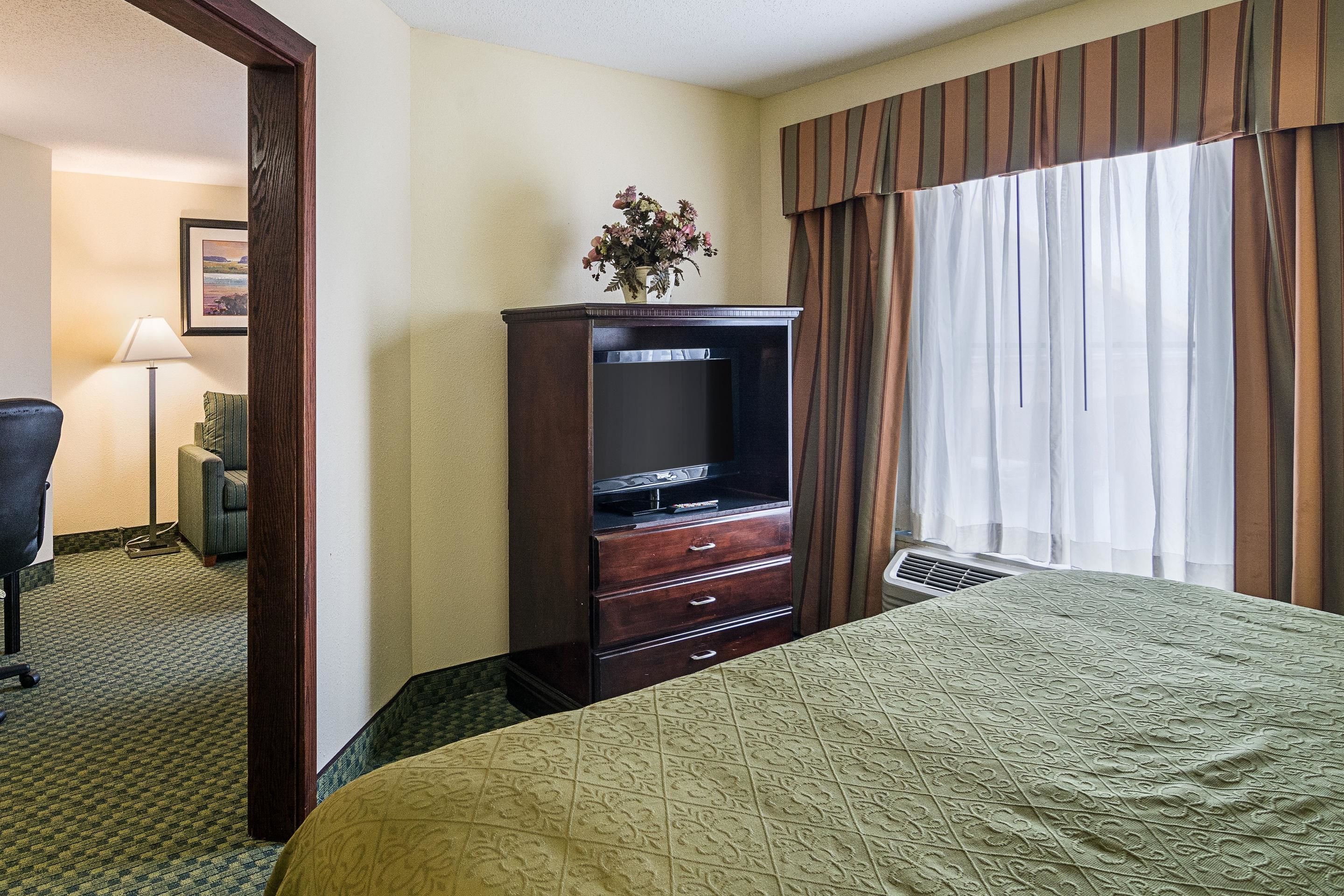 Une chambre d’hôtel comprenant un lit, une commode en bois avec un téléviseur à écran plat, un bureau et une chaise.