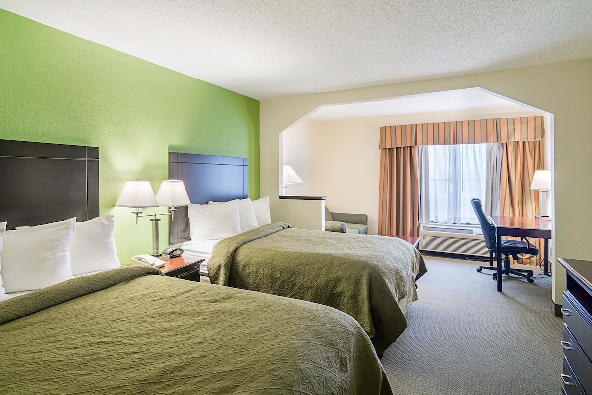 A hotel room with two beds, a desk, a chair, and a window with curtains.