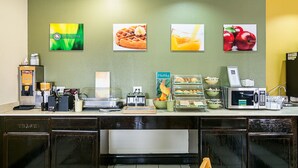 Um balcão de café da manhã com máquina de waffles, cafeteira e exposição de frutas.