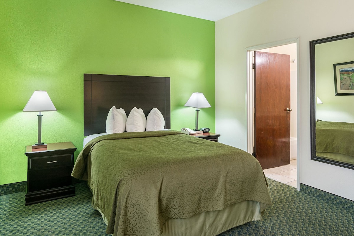 A hotel room with a green wall, a bed with a dark headboard, two bedside tables with lamps, and a door leading to another room.