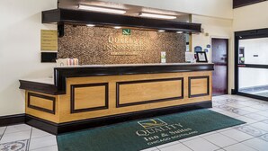 A reception desk at Quality Inn & Suites with a textured wall, a wooden counter, and a green mat with the hotel name. - Quality Inn & Suites Harvey - Chicago Southland (Harvey)