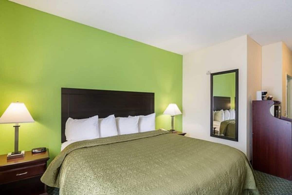 A hotel room with a bed, two bedside lamps, a dresser, and a mirror on the wall.