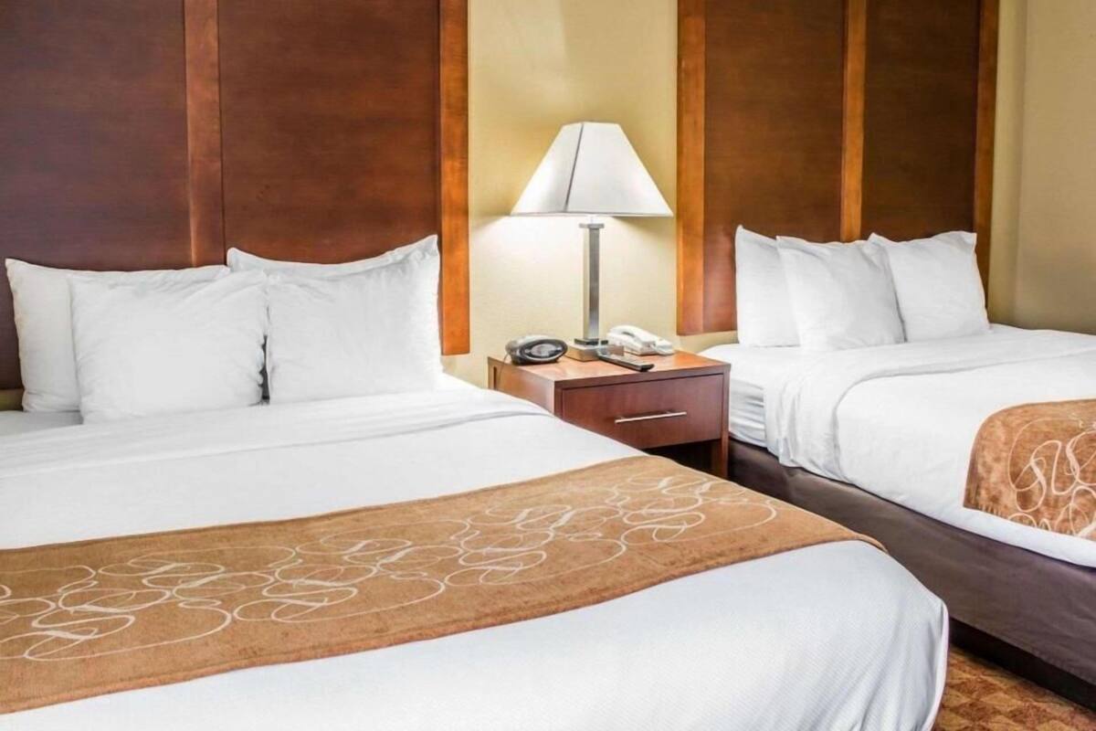 A hotel room with two beds, a nightstand with a lamp, and a wooden headboard.