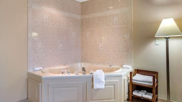 A bathroom with a freestanding bathtub, a wooden bench with towels, and a floor lamp.