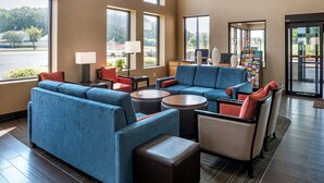 A spacious lobby with a blue sofa set, round coffee tables, and a seating area with red and beige chairs. Large windows provide natural light and a view of the outdoors. - Comfort Suites Hagerstown Southeast (Hagerstown)
