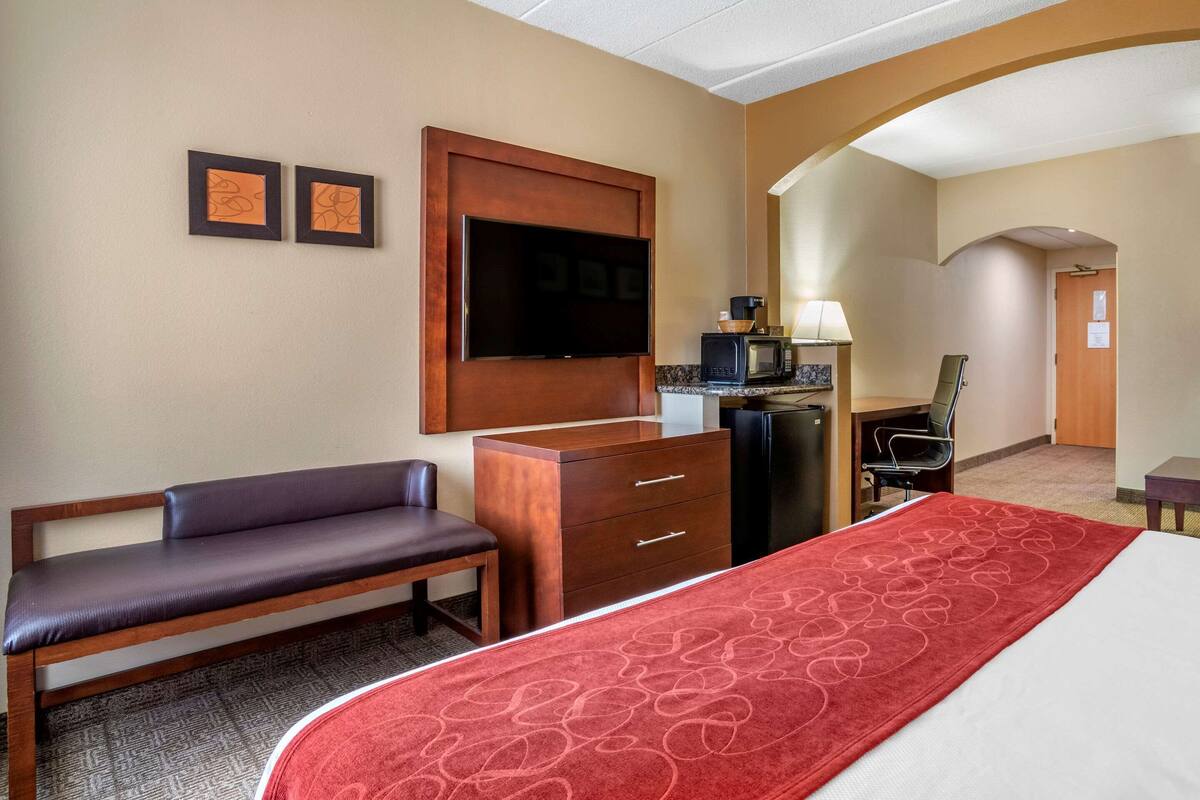 A hotel room with a bed, a desk, a chair, a television, and a microwave.