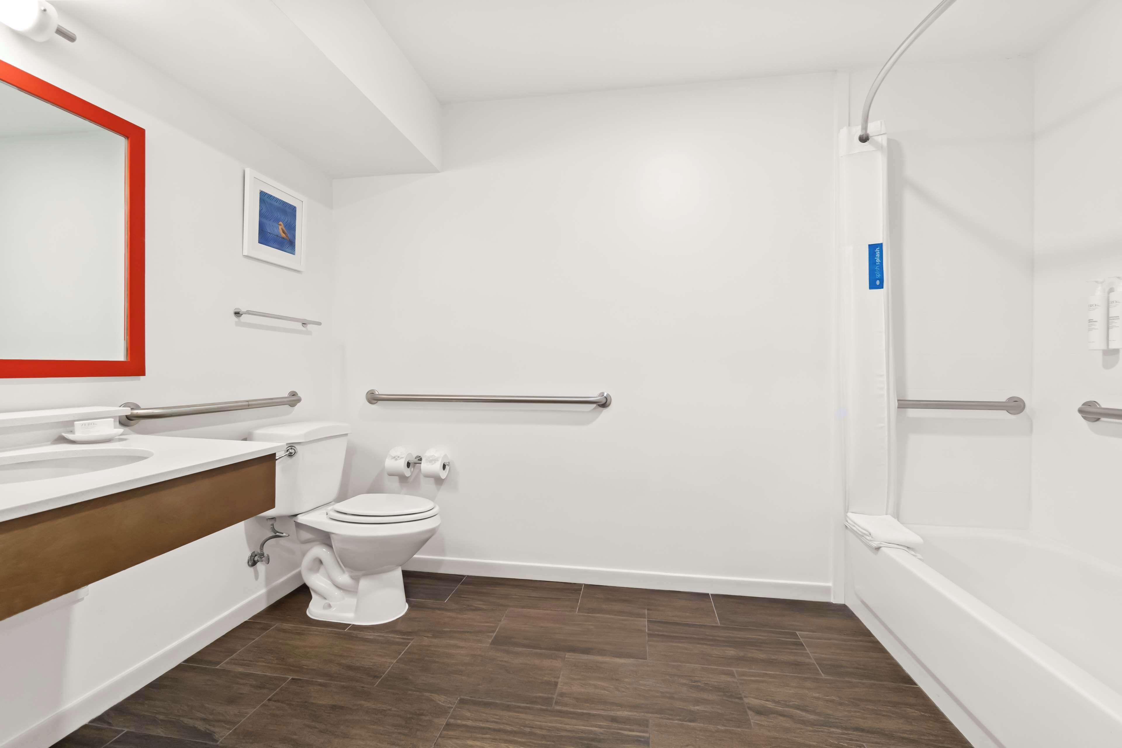 A modern bathroom with a white toilet, a sink with a wooden countertop, a shower with a glass door, and a handrail.