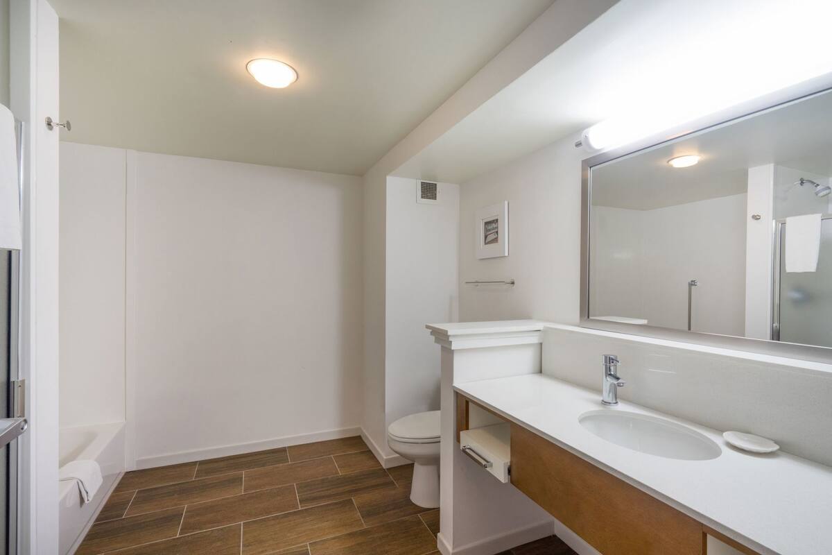 A bathroom with a white vanity, a mirror, a toilet, and a shower area.