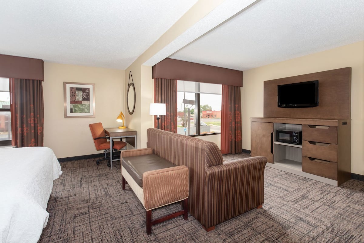 A hotel room with a bed, a desk with a chair, a sofa, a television, and a minibar.