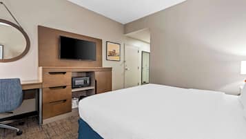 Habitación de hotel con una cama grande, un escritorio con silla, televisión de pantalla plana, microondas y puerta que da a un baño.