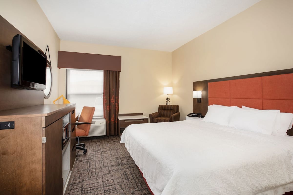A hotel room with a bed, desk, chair, TV, and a window with curtains.