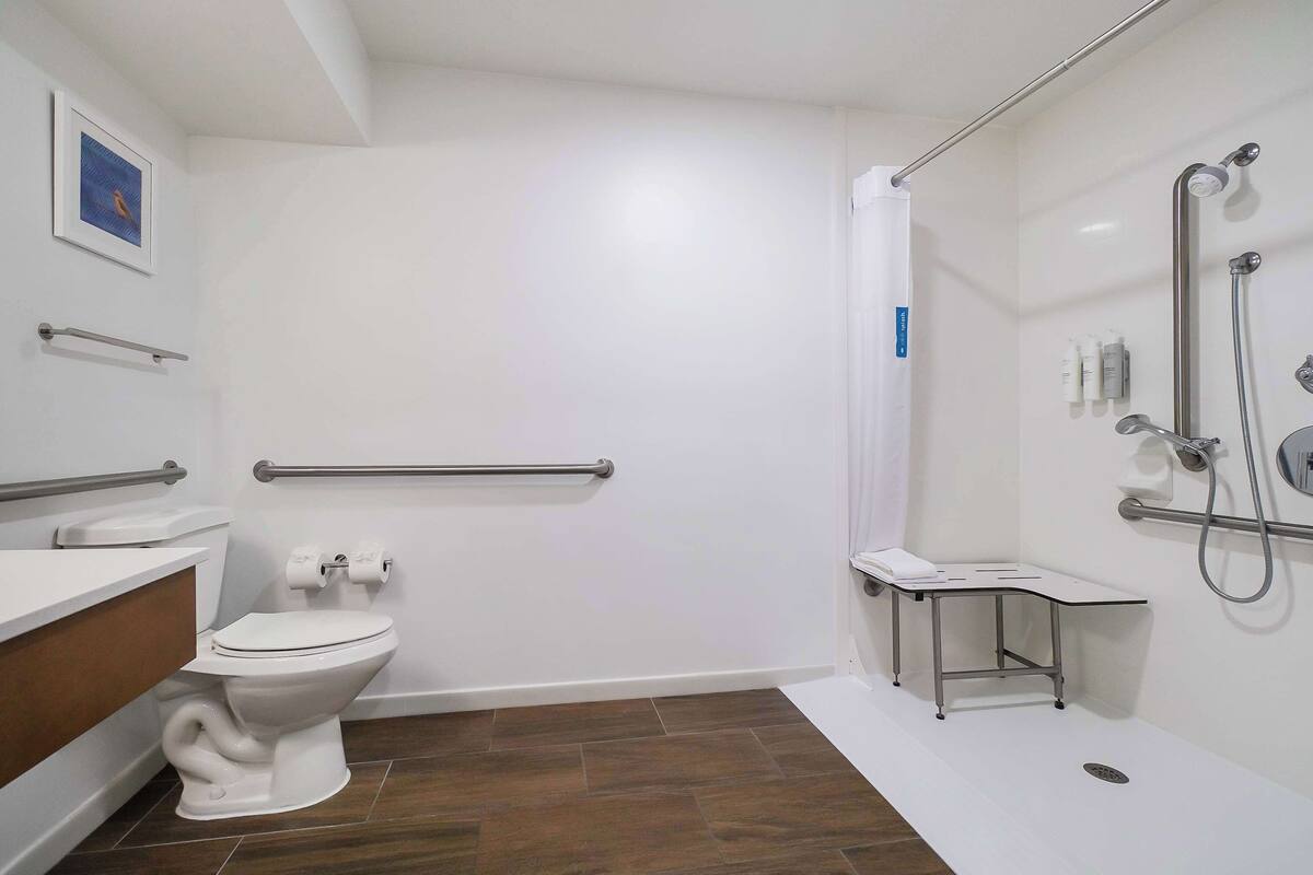 A bathroom with a toilet, a shower with grab bars, and a small table.