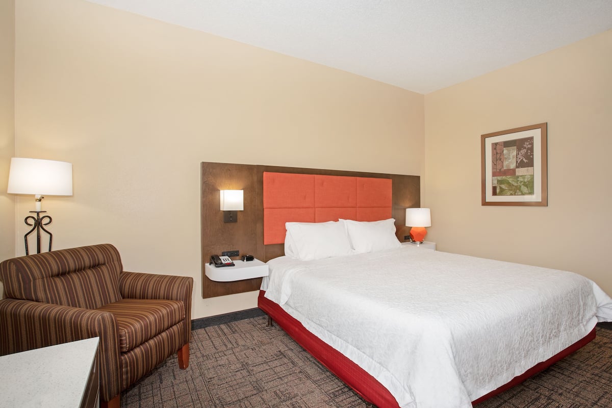 A hotel room with a bed, a chair, a nightstand, and a wall-mounted lamp.