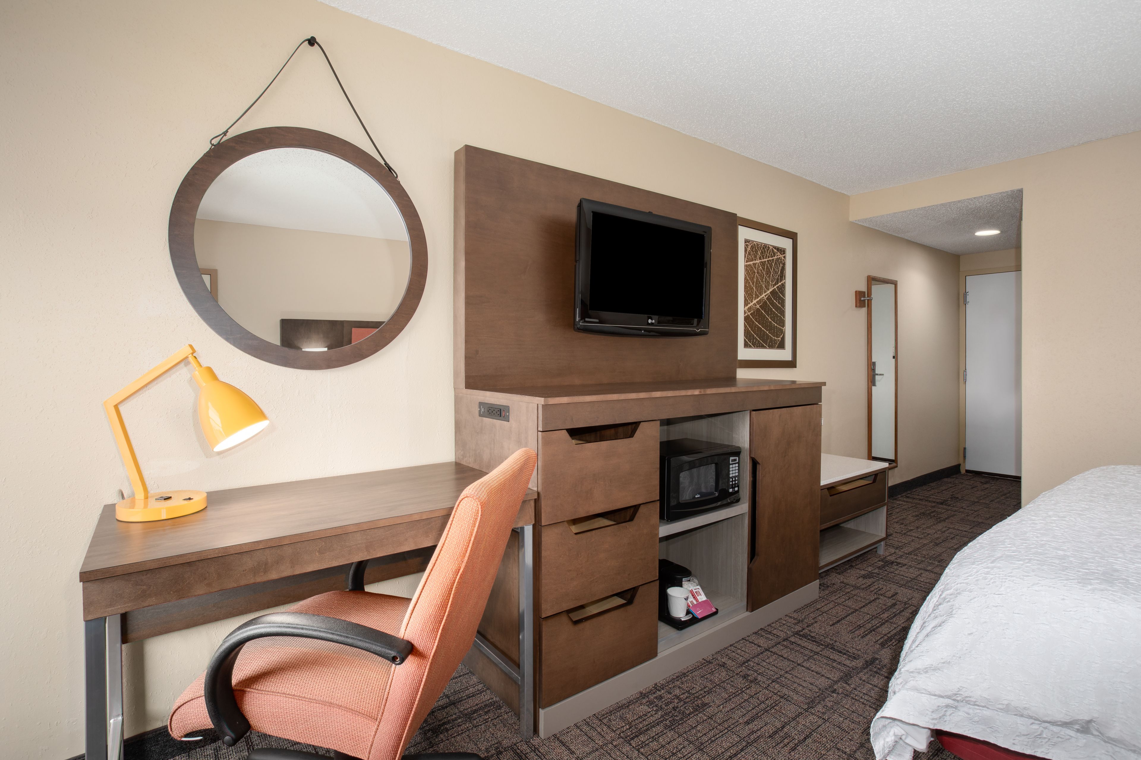 A hotel room with a desk, chair, TV, microwave, and a bed.