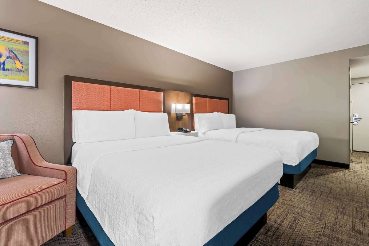 A hotel room with two beds, a desk, a chair, and a painting on the wall.