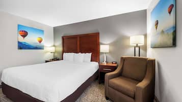A hotel room with a large bed, a wooden headboard, two bedside tables with lamps, a brown armchair, and two wall-mounted paintings of hot air balloons.