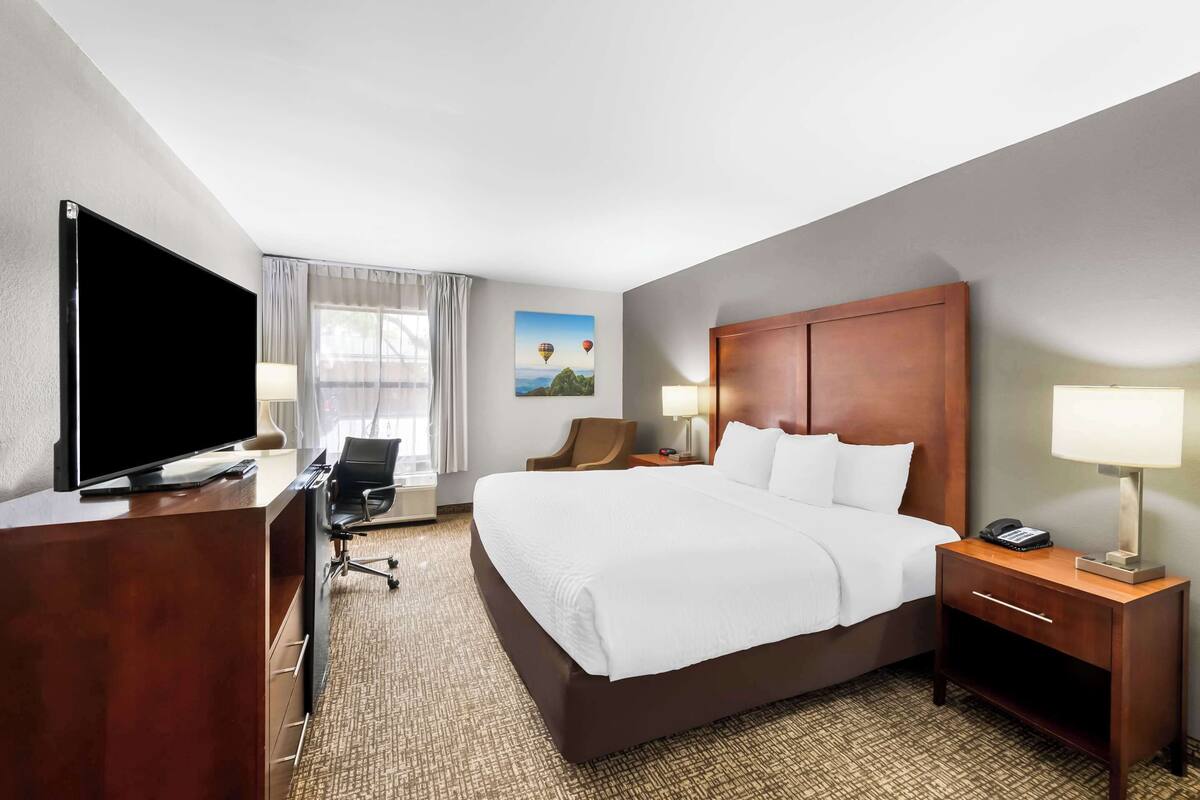 Une chambre d’hôtel avec un grand lit, un bureau doté d’un téléviseur à écran plat, une chaise, une lampe de bureau et une table de chevet avec une lampe.