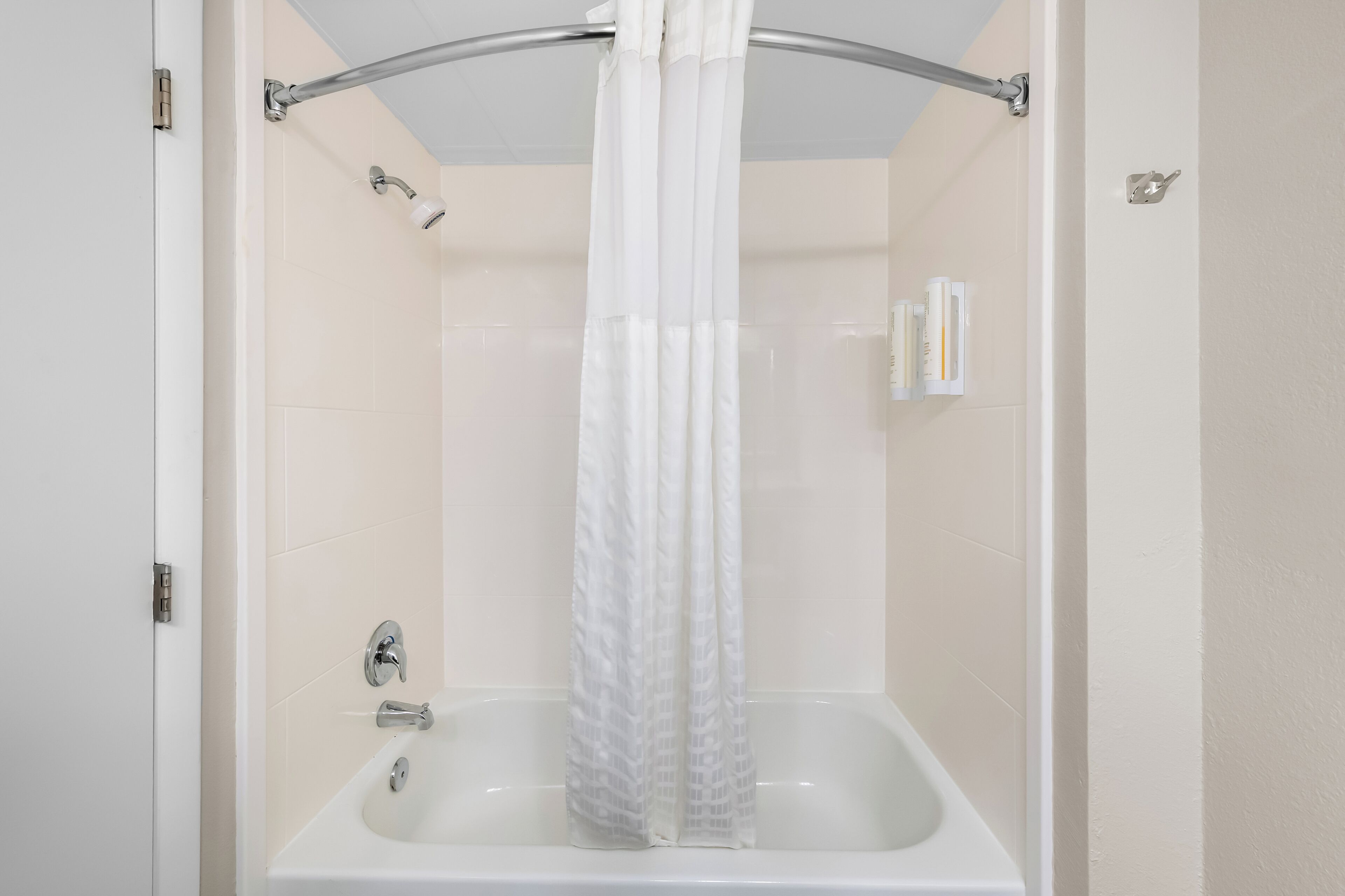A bathroom with a bathtub, a shower curtain, and a handrail.