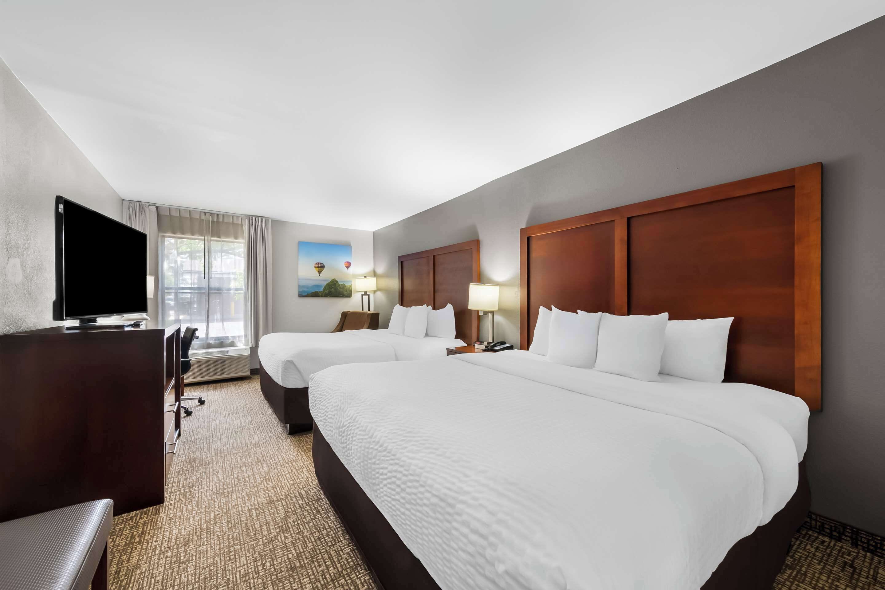A hotel room with two beds, a desk, a television, and a window with curtains.