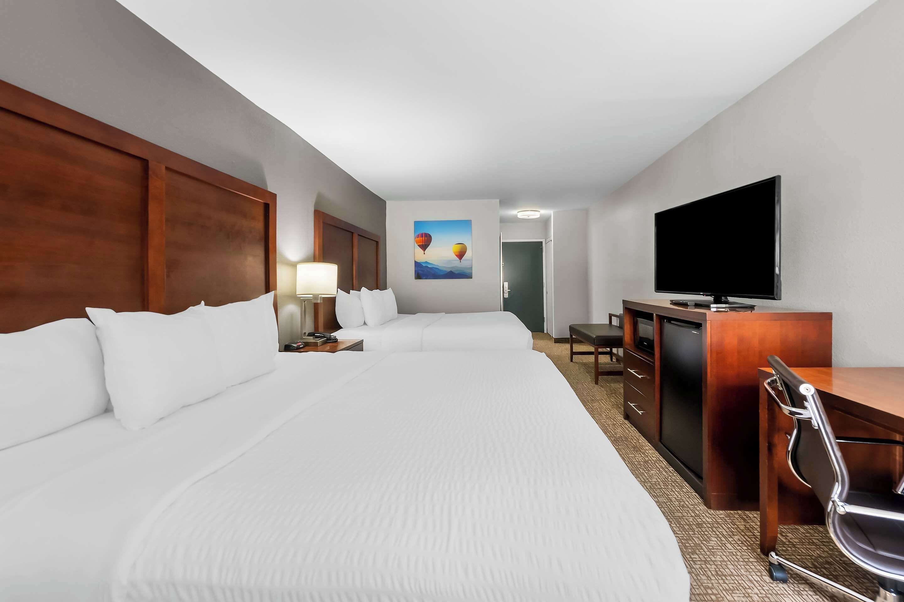 A hotel room with a large bed, a desk with a TV, and a painting on the wall.