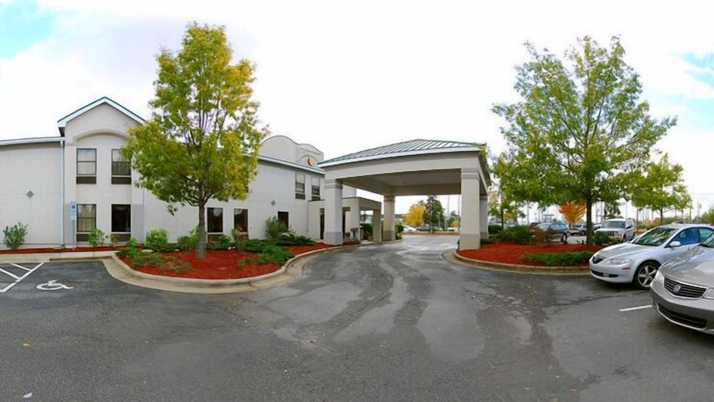 A building with a covered entrance, parking lot, and trees.