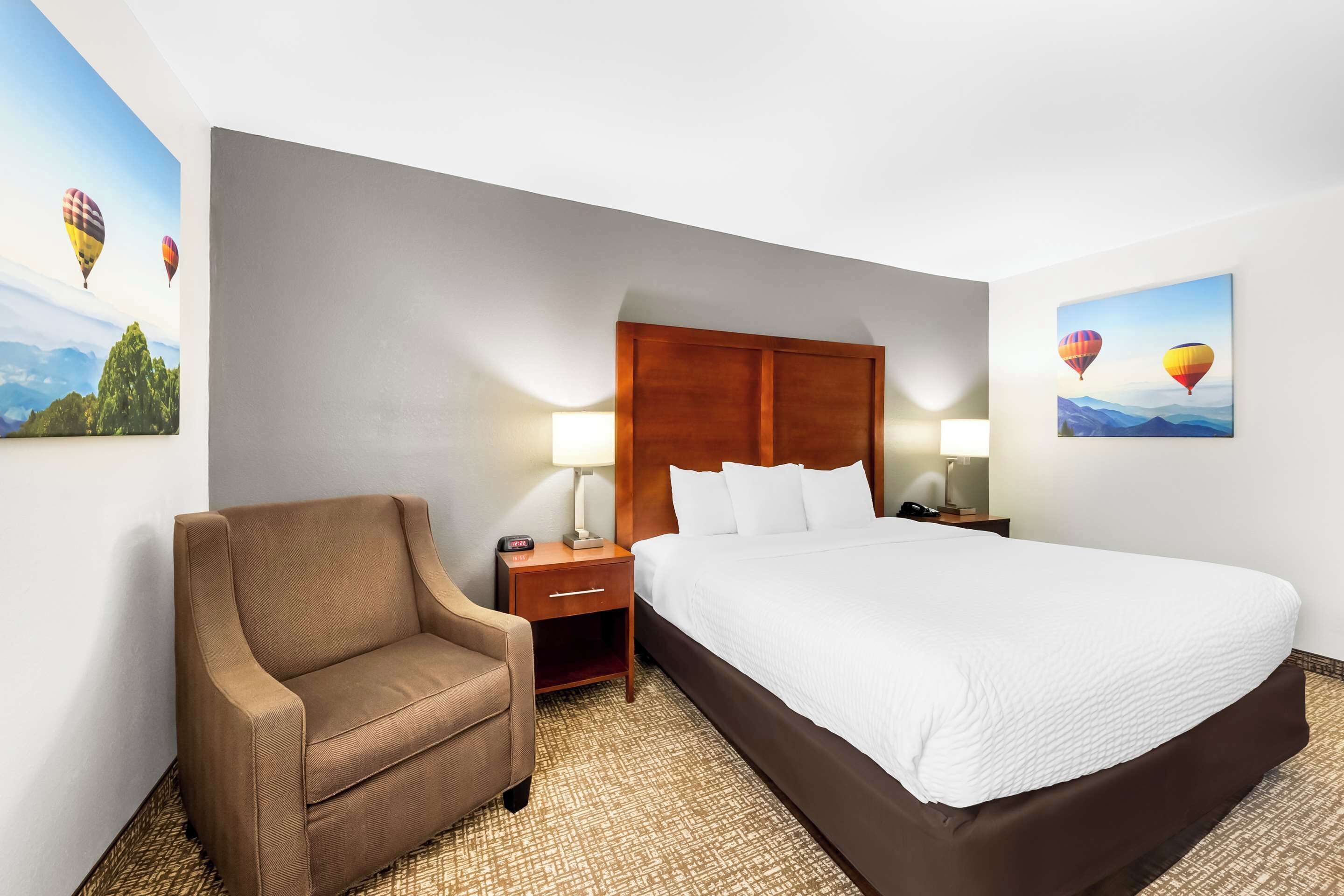Een hotelkamer met een bed, een stoel, een nachtkastje en twee wandlampen.