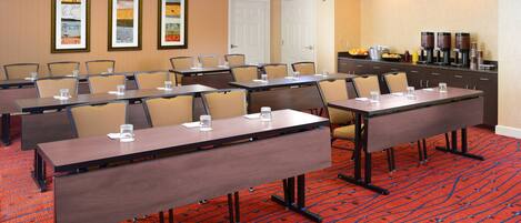 A conference room with multiple tables and chairs, a coffee station, and framed artwork on the walls.