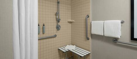 A modern bathroom with a shower, grab bars, a bench, and a towel rack.