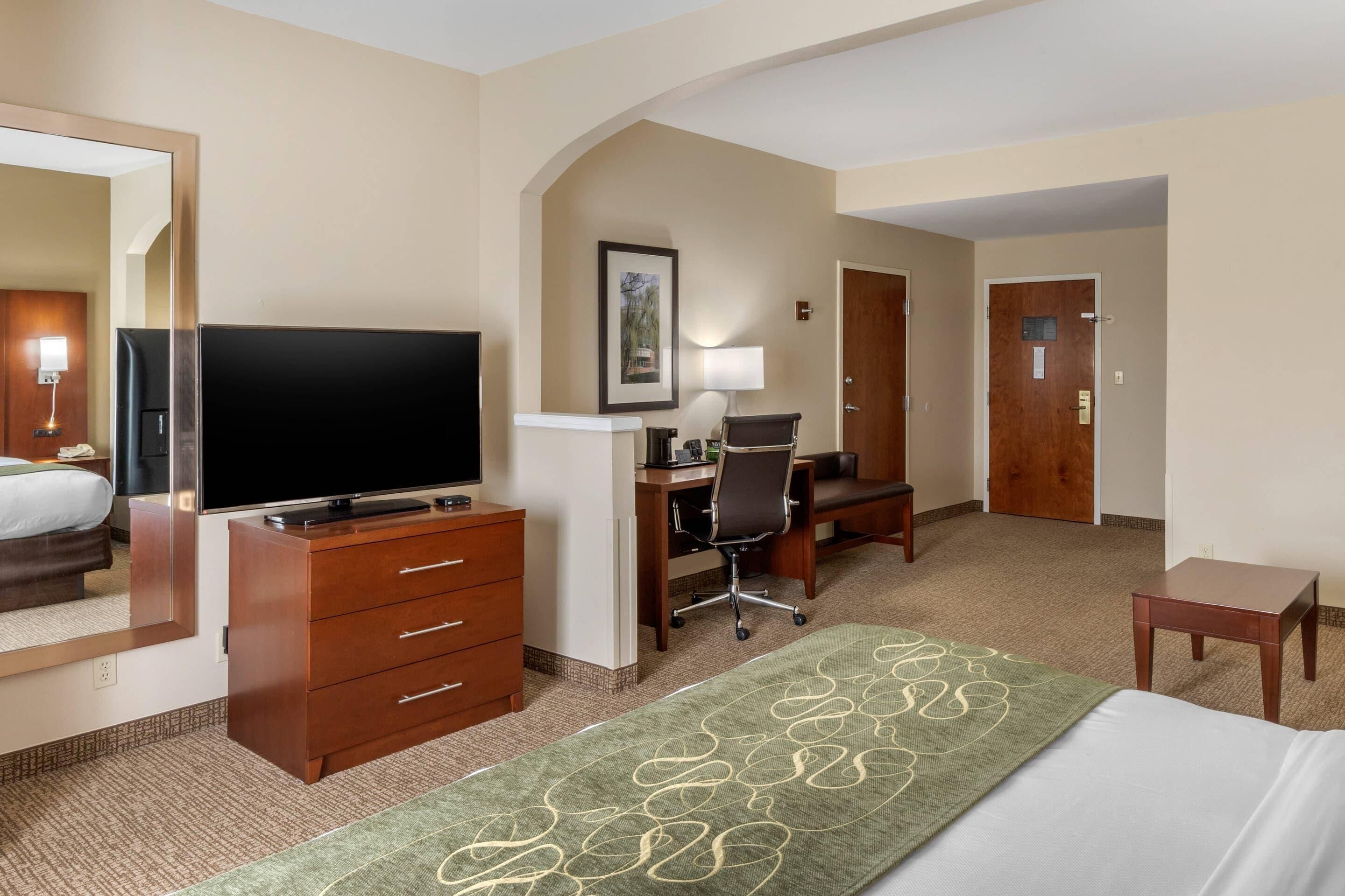 Une chambre d’hôtel comprenant un lit, une télévision, un bureau avec une chaise, une commode et un tapis.