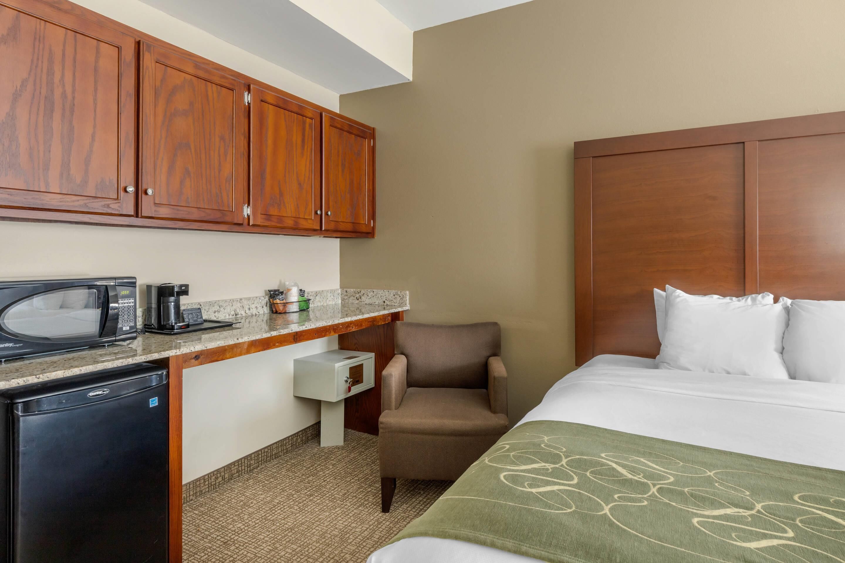 A hotel room with a bed, a chair, a desk with a microwave, a coffee maker, and a small refrigerator.