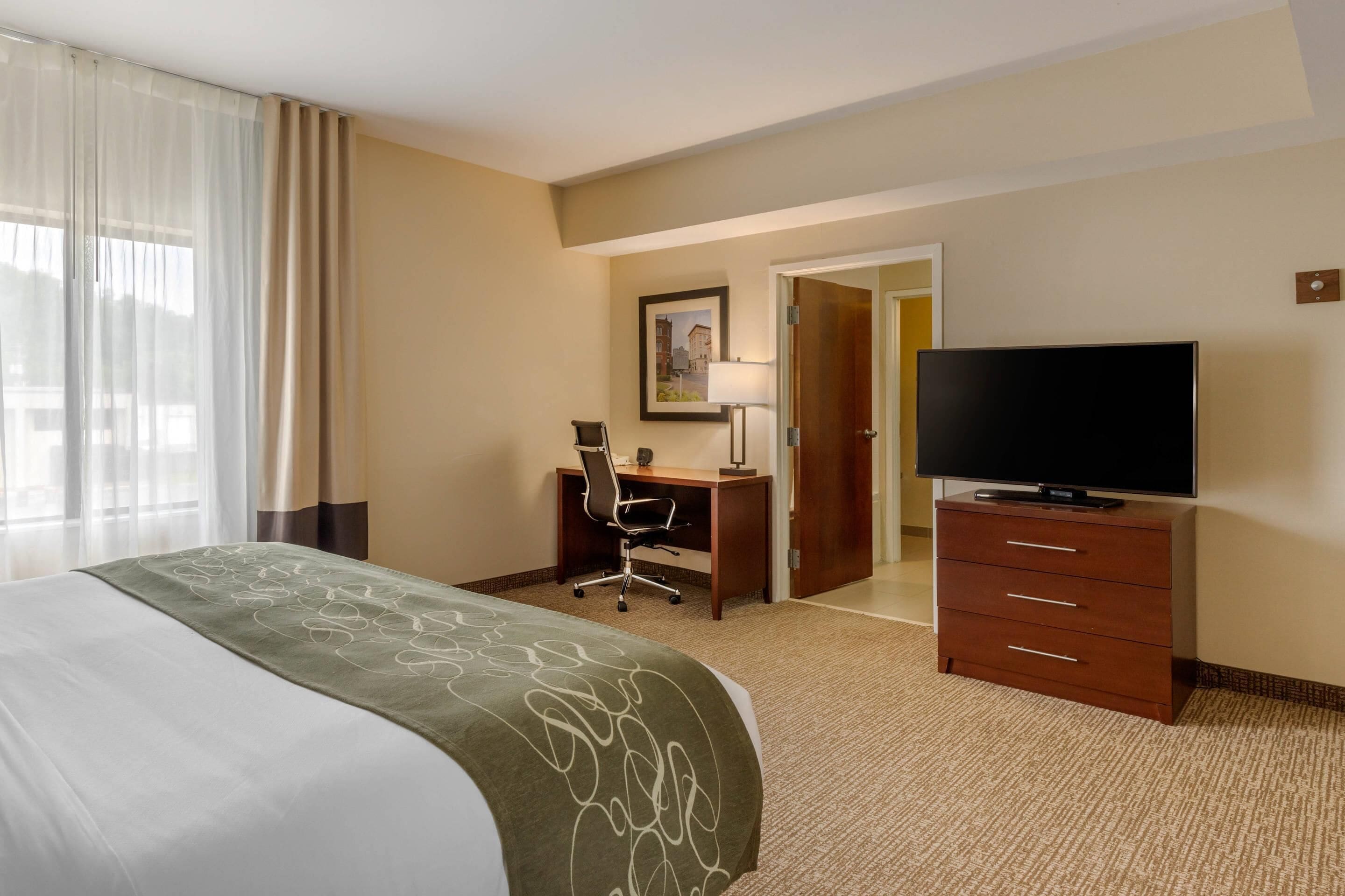 Une chambre d’hôtel comprenant un lit, un bureau, une télévision et une porte donnant sur une autre pièce.