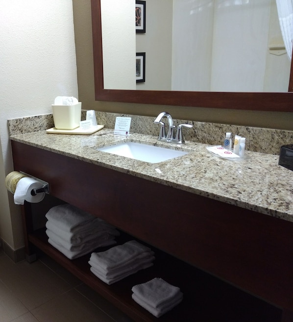 A hotel bathroom with a granite countertop, a sink, a mirror, and a towel rack with folded towels. - Comfort Suites Johnson City near University (Johnson City)