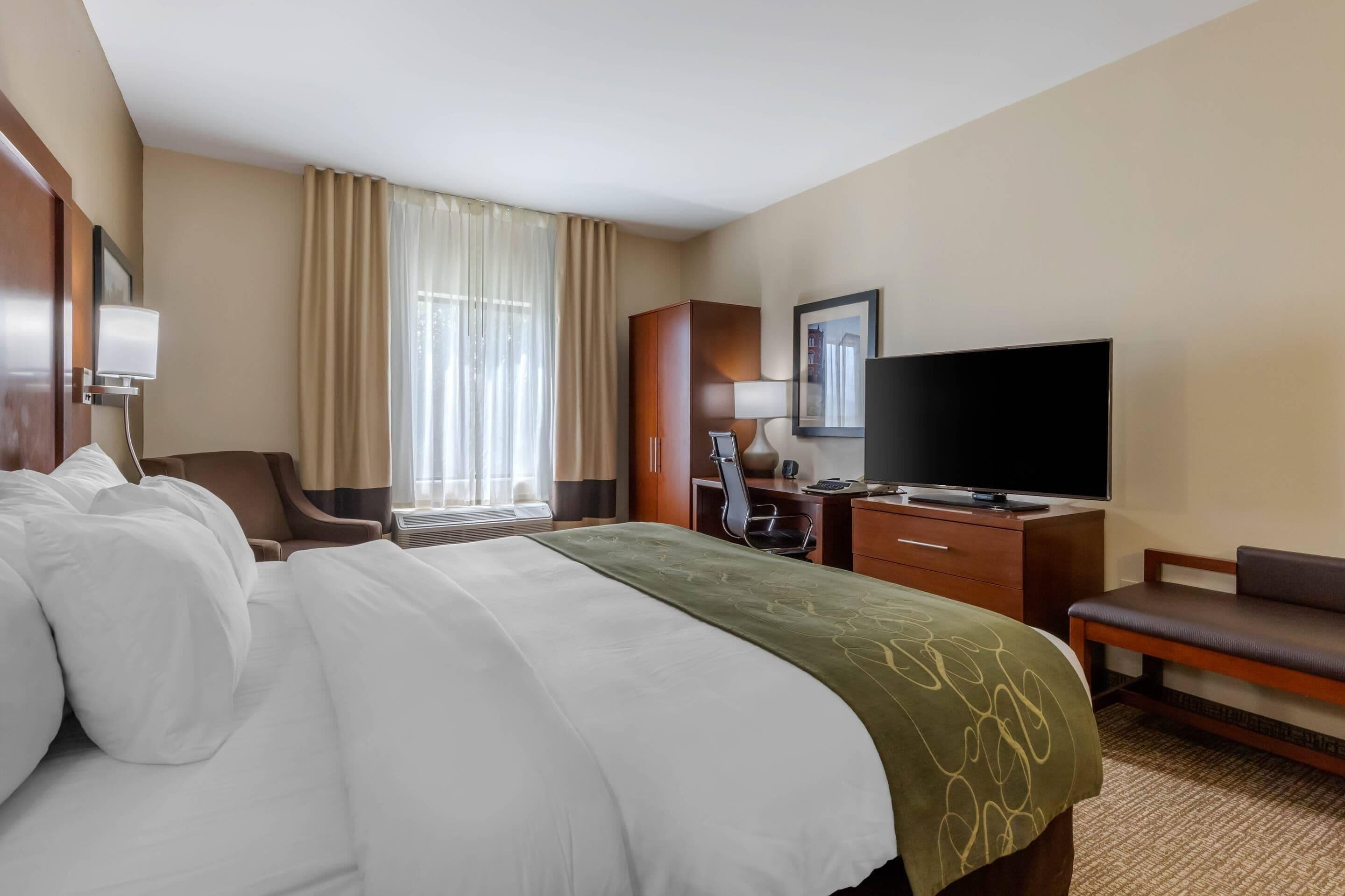 A hotel room with a large bed, a desk with a chair, a television, and a window with curtains.