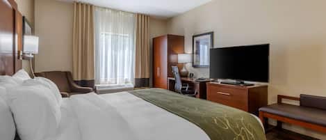 A hotel room with a large bed, a desk with a chair, a television, and a window with curtains.
